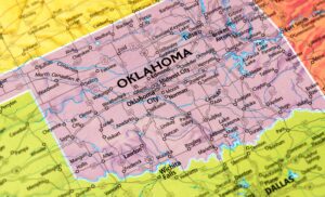 A close-up map of Oklahoma shows major cities, including Oklahoma City, Tulsa, and Norman, with surrounding states partially visible, such as Texas and Kansas. The state name OKLAHOMA is printed in large letters.