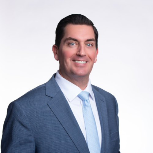 Ryan Bingham - Sullivan and LeShane Inc A man in a blue suit, white shirt, and light blue tie smiles at the camera against a plain white background.