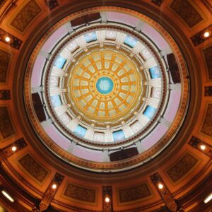 Looking up at an ornate domed ceiling with gold, white, and blue patterns, surrounded by decorative architectural details and warm lighting.